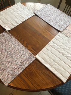 four pieces of cloth laid out on top of a wooden table with chairs in the background