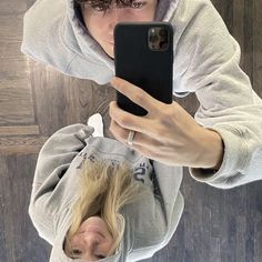 a woman taking a selfie with her cell phone in front of her head and wearing a hoodie