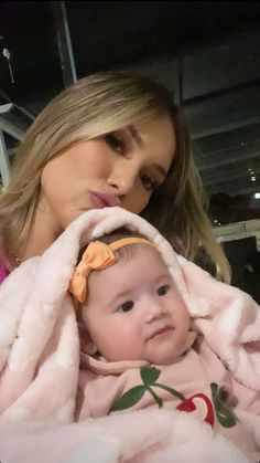 a woman is holding a baby wrapped in a pink blanket and looking at the camera