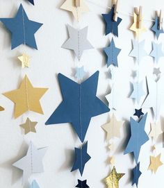 some blue and gold stars hanging from clothes pins on a white wall with pegs