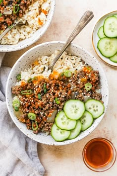 two bowls filled with rice and cucumbers next to some sauce on the side