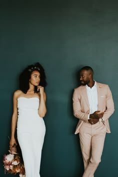 a man and woman standing next to each other in front of a green wall with flowers