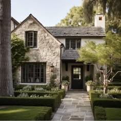 a stone house with hedges and trees in the front yard