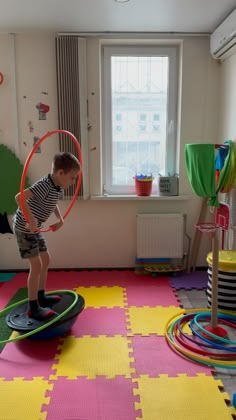 a young boy standing on top of a hula hoop in a room with toys