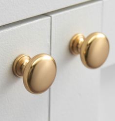 two gold knobs on the handles of a white cabinet