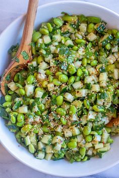 a white bowl filled with green vegetables next to a wooden spoon on top of a table