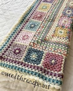 a crocheted blanket is laying on top of a white bed spread with colorful squares