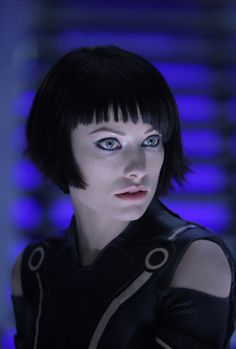 a woman with short black hair and blue eyes in a futuristic outfit looking at the camera