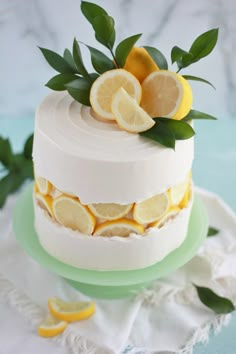 a white cake with lemons and leaves on top sitting on a green platter