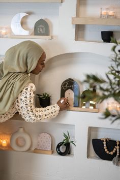 a woman in a headscarf is decorating shelves with candles and plants on them