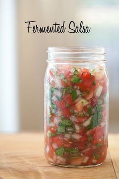 a jar filled with tomatoes, onions and other vegetables on top of a wooden table