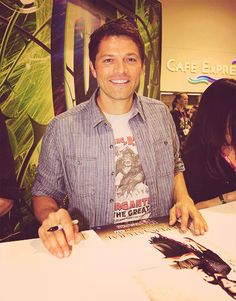 a man sitting at a table in front of a book signing an autographed photo