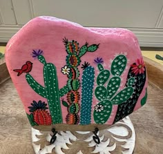 a pink rock with cactus designs on it sitting on top of a wooden table next to a potted plant