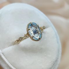 an oval shaped blue topaz ring sits in a white velvet case