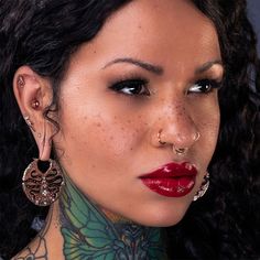 a woman with tattoos and piercings on her neck is looking at the camera while wearing red lipstick