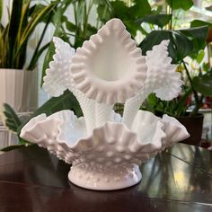 three white vases sitting on top of a wooden table next to potted plants