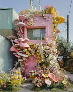 a pink house with lots of flowers and plants on the front door is covered in fake mushrooms