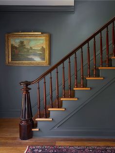 a painting hangs on the wall next to a stair case in a blue painted room