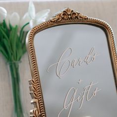 a close up of a mirror on a table with flowers in front of it and a vase behind it