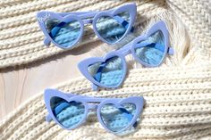 three pairs of blue sunglasses sitting on top of a white sweater