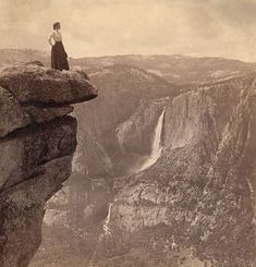 a woman standing on top of a cliff with a waterfall in the backgroud