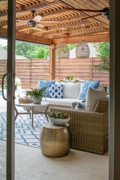 an outdoor living area with wicker furniture and blue pillows on the couches, in front of a wooden pergoline