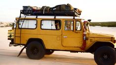 an old yellow truck with luggage on top driving down the road in the sand dunes