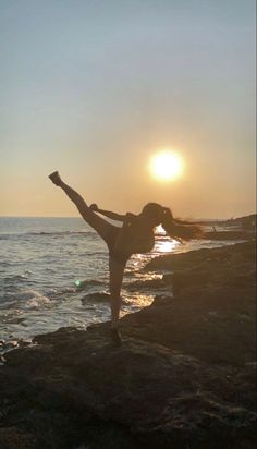 a woman standing on top of a rocky beach next to the ocean with her arms in the air