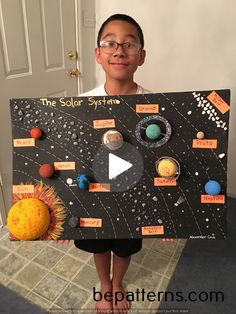 a young boy is holding up a solar system board with planets and sun on it