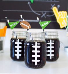 three mason jars filled with black liquid and decorated with football pennants on them, sitting on a table