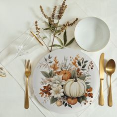 a place setting with pumpkins, flowers and goldware on a white table cloth