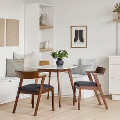 two chairs and a table in a room with white walls, wood flooring and open shelving