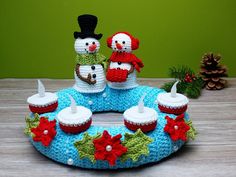 two knitted snowmen sitting on top of a blue cake with candles in it