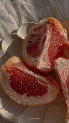 three grapefruits on a white plate sitting on a tablecloth covered table