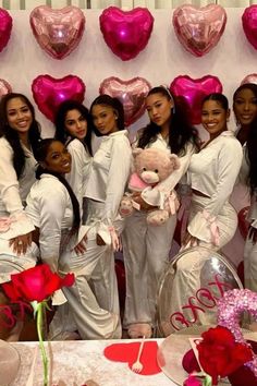 a group of women standing next to each other in front of balloons and heart shapes