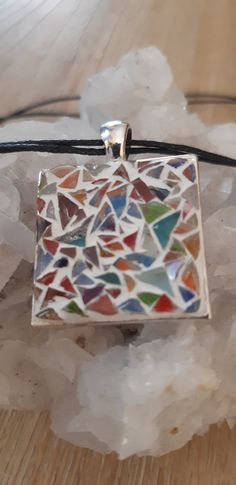 a small square pendant with multicolored glass tiles on it sitting on a table