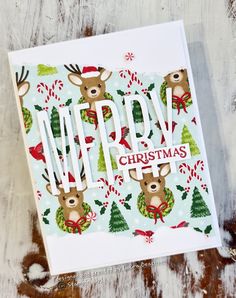 a merry christmas card with reindeer and candy canes on it, sitting on a wooden surface