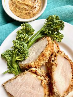 some meat and broccoli on a white plate next to a bowl of sauce