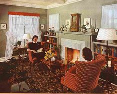 two women sitting in chairs in a living room with a fireplace and bookshelf