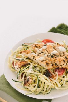 a white plate topped with pasta and chicken on top of a green napkin next to a fork