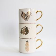 three coffee mugs stacked on top of each other with gold rims and designs