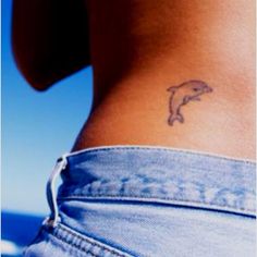 a woman with a dolphin tattoo on her lower back and the ocean in the background