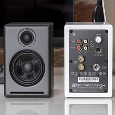 two speakers sitting next to each other on top of a white table with a computer monitor in the background