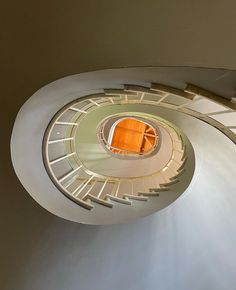 an overhead view of a spiral staircase with orange chairs in the center and white walls