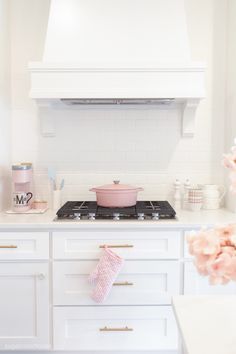 a stove top oven sitting inside of a kitchen next to white cabinets and pink flowers