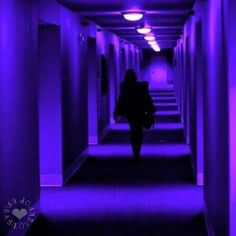 a person walking down a long hallway with purple lights