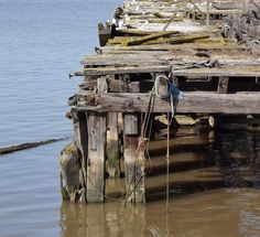 an old wooden dock sitting in the middle of a body of water with ropes hanging from it's posts