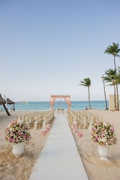 an outdoor ceremony set up on the beach with chairs and flowers in front of it