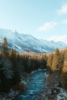 a river running through a forest filled with snow covered mountains in the distance are pine trees and evergreens