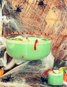 a green halloween drink in a glass with candy on the rim and spooky spider web around it